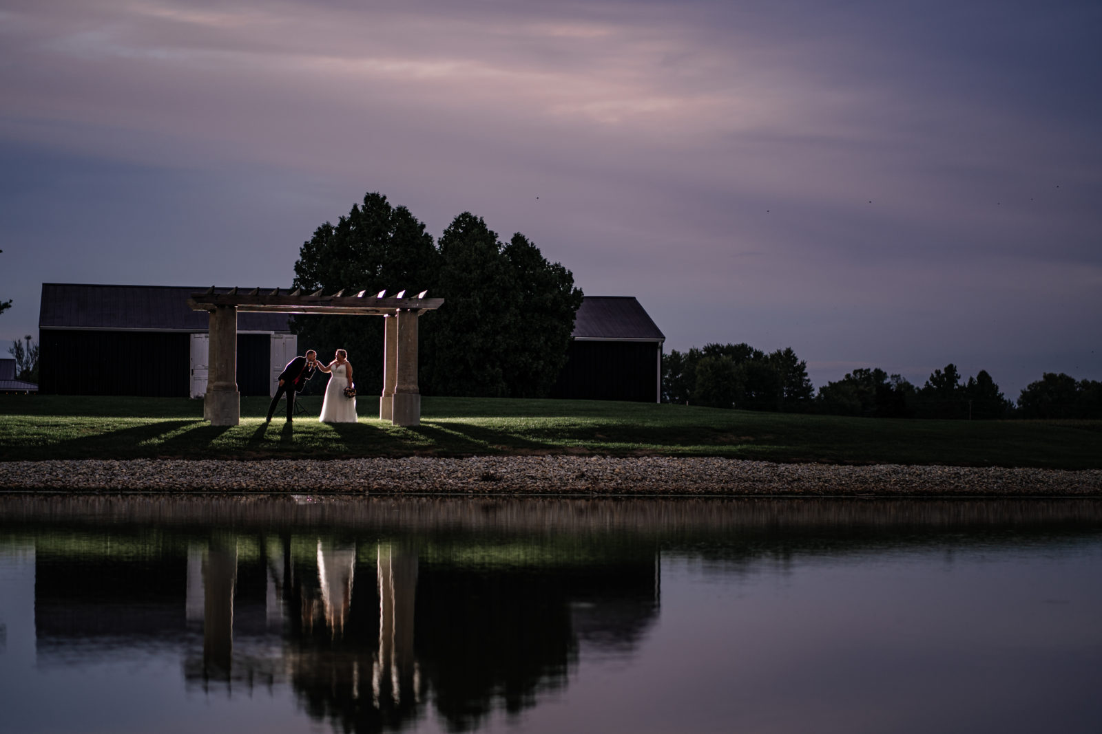 bride and groom backlit across pond at dusk 